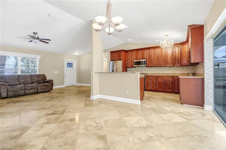 Kitchen with ceiling fan with notable chandelier, appliances with stainless steel finishes, decorative light fixtures, backsplash, and light tile flooring