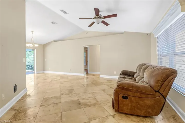 Sitting room with lofted ceiling, light tile floors, and ceiling fan with notable chandelier