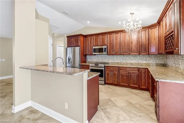 Kitchen featuring backsplash, appliances with stainless steel finishes, a chandelier, and light tile floors
