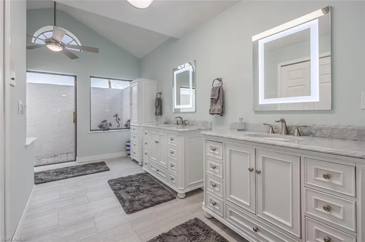 Bathroom featuring two vanities, vaulted ceiling, walk in shower, ceiling fan, and light wood-style flooring