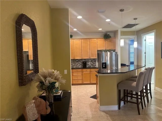 Kitchen featuring decorative backsplash, a kitchen breakfast bar, stainless steel fridge, hanging light fixtures, and light tile patterned floors