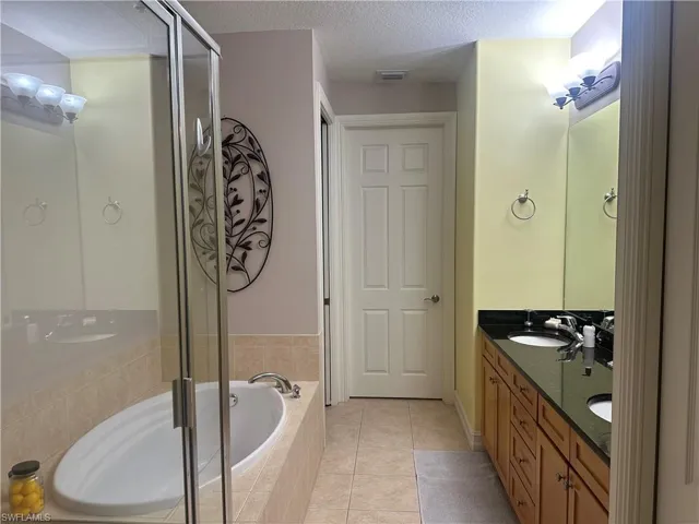 Bathroom with light tile patterned floors, a textured ceiling, a bath, double vanity, and a shower stall