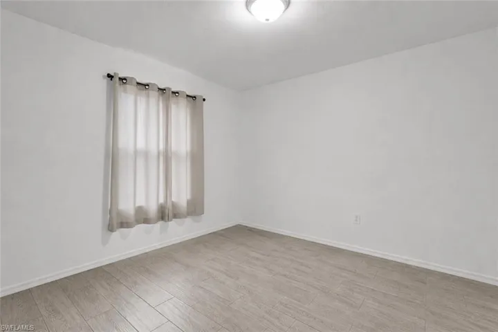 Bright interior space featuring light wood-finish flooring, white baseboards, and a flush-mount ceiling light
