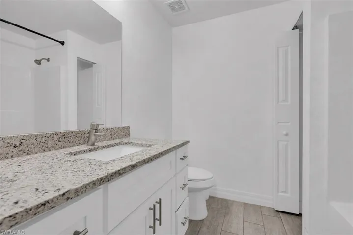 Bathroom featuring a white vanity with an undermount sink, speckled countertop, and brushed nickel faucet