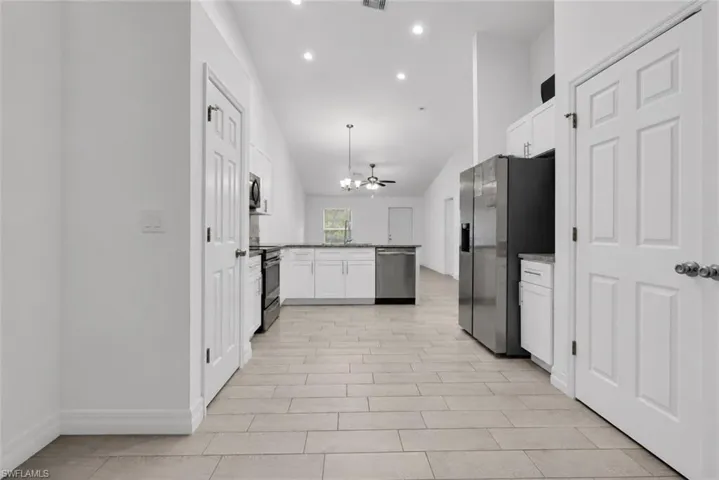 Open-concept kitchen with white cabinetry, stainless steel appliances, and light-toned tile flooring