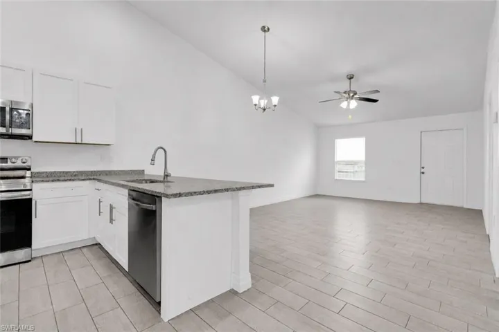 Open-concept living space with vaulted ceilings, featuring a kitchen with white cabinetry, stainless steel appliances, and a peninsula with a dark speckled countertop