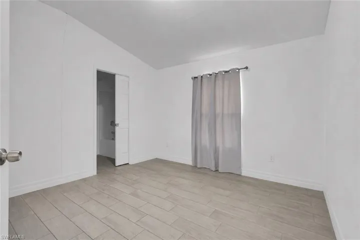 Spacious room featuring light-toned wood-finish tile flooring, clean white walls, and white baseboards