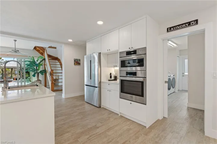 Kitchen with stainless steel appliances, white cabinets, independent washer and dryer, and light wood look tile flooring