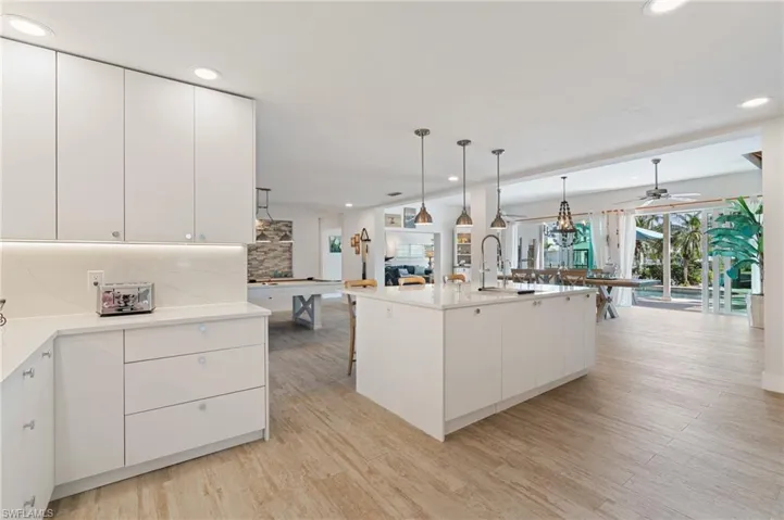Kitchen with decorative light fixtures, wood look tile flooring, an island with sink, decorative backsplash, and white cabinets