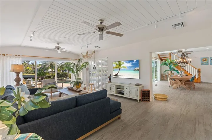 Living room featuring wood look tile floors, ceiling fan with notable chandelier, vaulted ceiling, and rail lighting