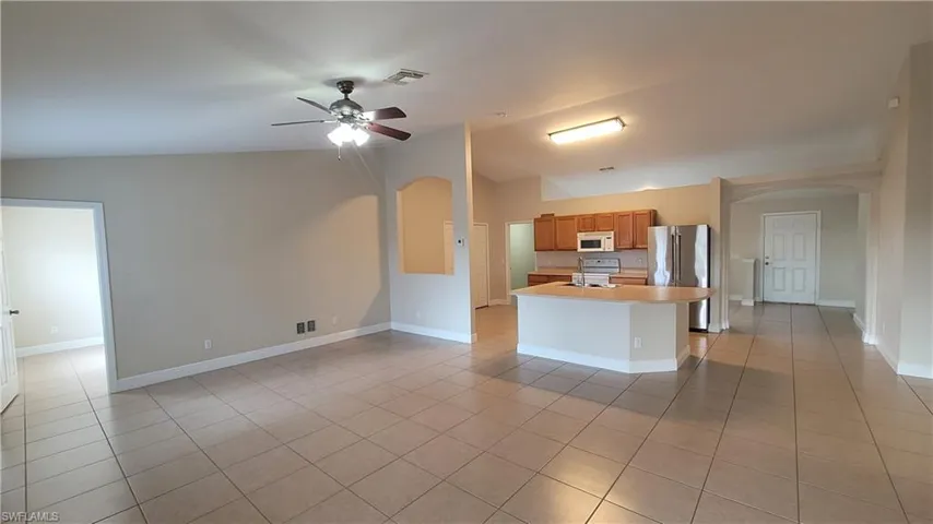 Kitchen with arched walkways, a kitchen island with sink, ceiling fan, wood finish cabinetry, and lofted ceiling