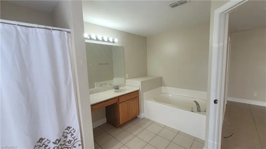 Full bathroom featuring light tile patterned floors, a bath, vanity, and a shower with shower curtain
