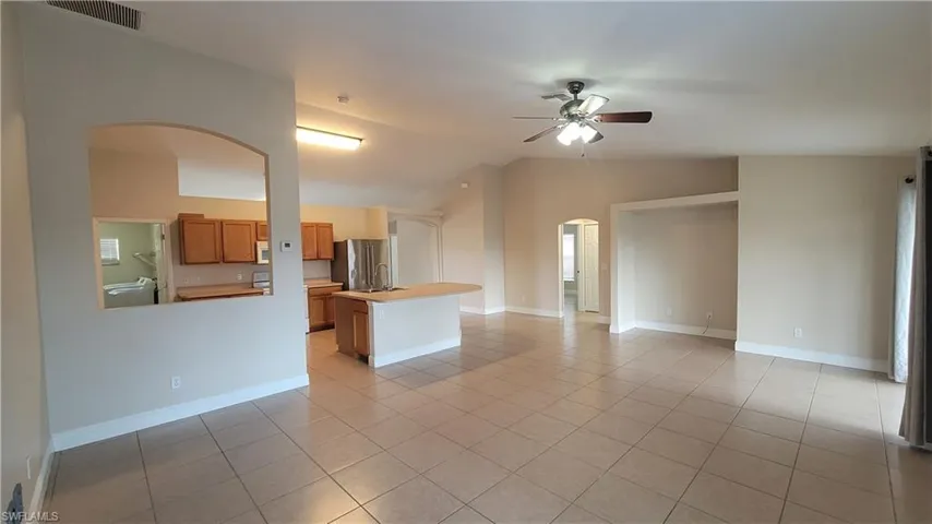 Unfurnished living room featuring arched walkways, a ceiling fan, lofted ceiling, light tile patterned flooring, and washer / dryer