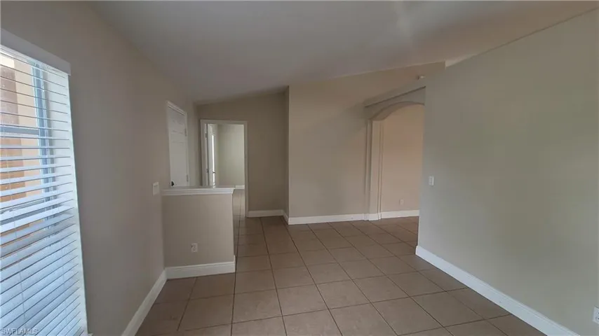 Spare room featuring arched walkways, light tile patterned flooring, and vaulted ceiling