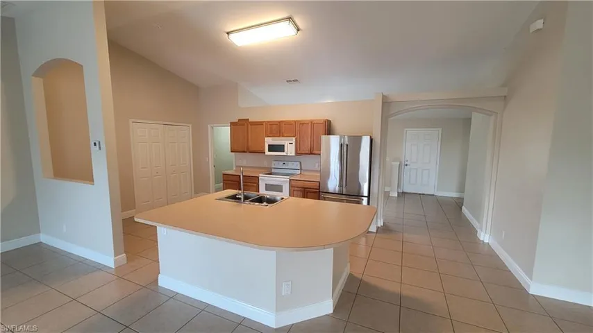 Kitchen with arched walkways, white appliances, light countertops, lofted ceiling, and wood finish cabinetry