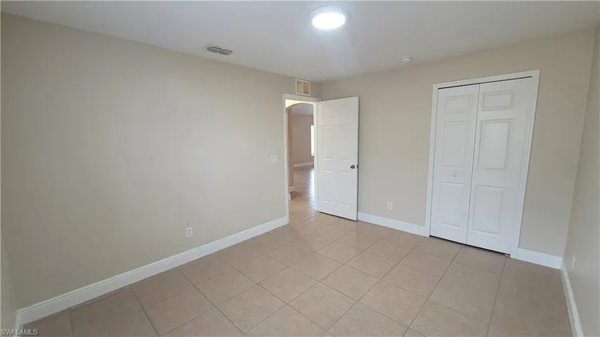 Unfurnished bedroom with light tile patterned flooring, arched walkways, and a closet