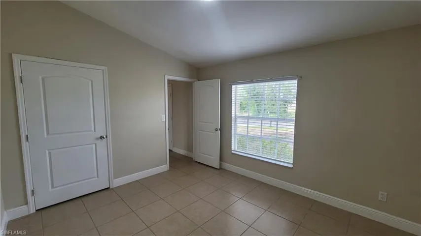 Unfurnished bedroom with vaulted ceiling and light tile patterned floors