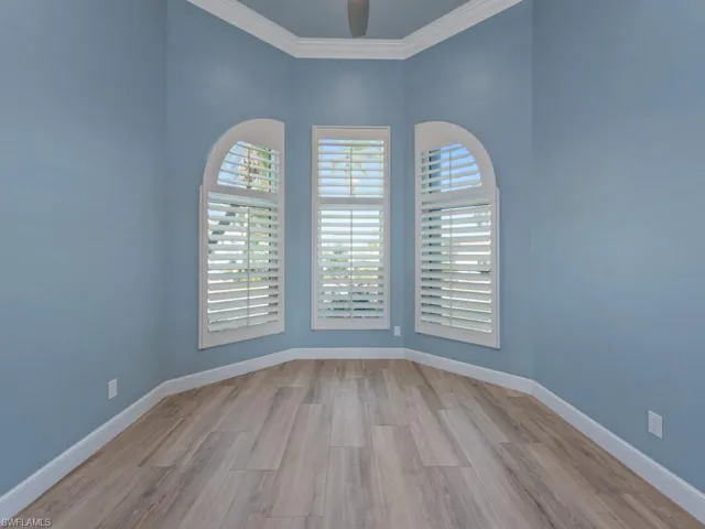 Unfurnished room featuring a ceiling fan, ornamental molding, baseboards, and wood finished floors