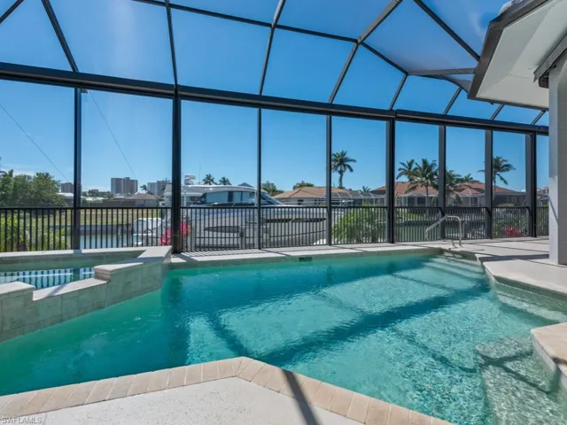 View of swimming pool featuring glass enclosure, a pool with connected hot tub, and a patio area