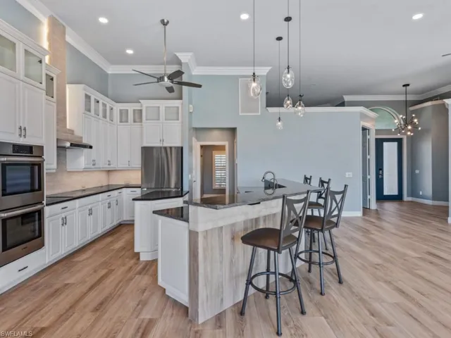 Kitchen featuring a kitchen bar, stainless steel appliances, ceiling fan with notable chandelier, an island with sink, and light wood finished floors