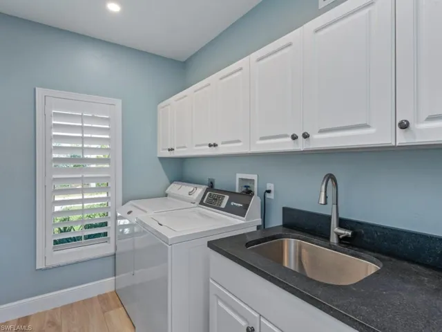 Laundry area with a sink, washing machine and clothes dryer, light wood-style flooring, baseboards, and cabinet space