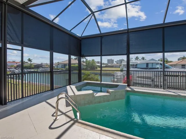 View of pool featuring glass enclosure, a pool with connected hot tub, a water view, and a patio area