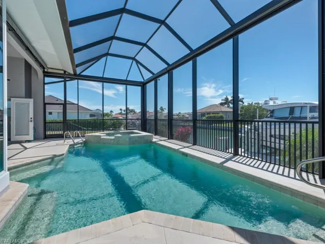 View of swimming pool featuring glass enclosure, a pool with connected hot tub, and a patio