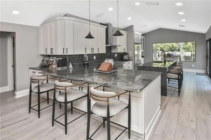 Kitchen featuring tasteful backsplash, vaulted ceiling, pendant lighting, kitchen peninsula, and light wood-type flooring