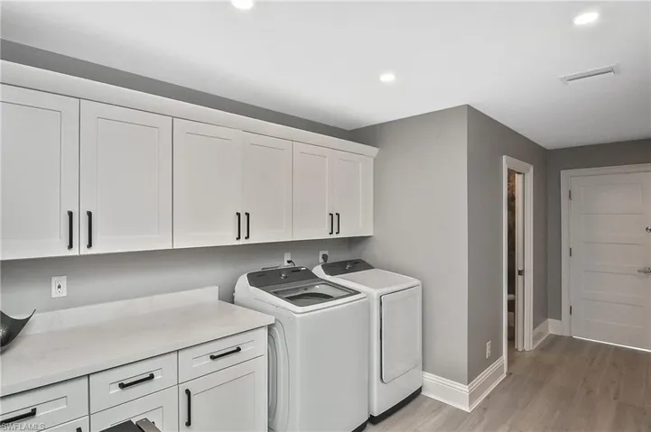 Laundry area with light hardwood / wood-style flooring, washer and dryer, and cabinets