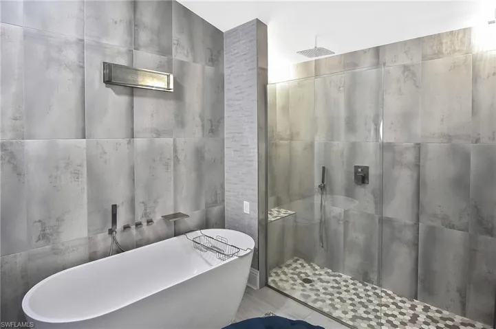 Bathroom featuring tile patterned flooring, tile walls, and separate shower and tub