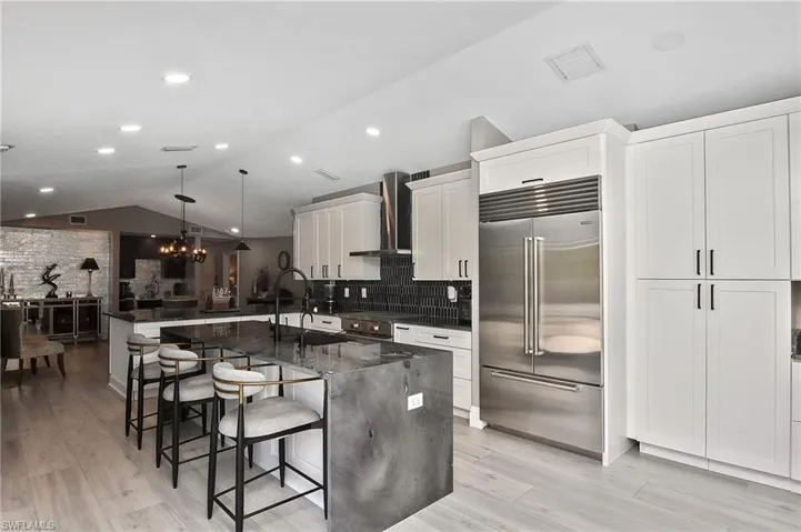 Kitchen with hanging light fixtures, wall chimney exhaust hood, a center island with sink, lofted ceiling, and high quality appliances