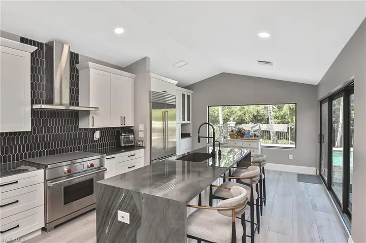Kitchen with backsplash, an island with sink, high quality appliances, and wall chimney range hood