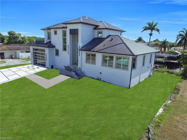 Rear view of property featuring a standing seam roof, concrete driveway, stucco siding, and a garage