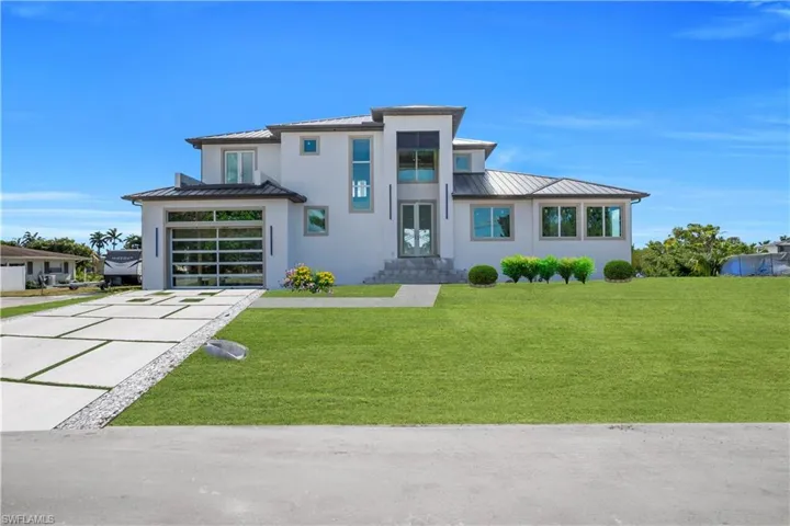 View of front of property with a standing seam roof, a front lawn, driveway, and stucco siding