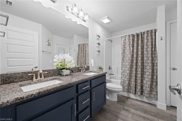 Bathroom with shower / bathtub combination with curtain, double vanity, and dark wood-style floors