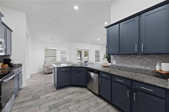 Kitchen featuring backsplash, dark stone countertops, a peninsula, wood finish floors, and stainless steel appliances