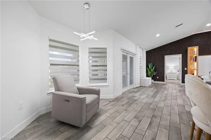 Sitting room featuring wood tiled floors, an accent wall, vaulted ceiling, wallpapered walls, and a chandelier