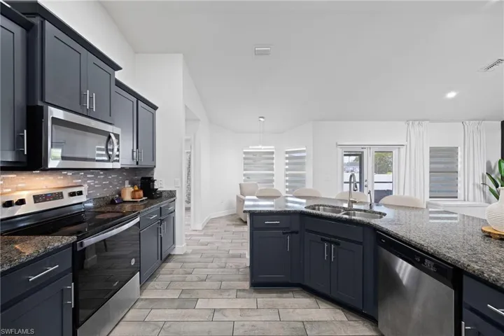 Kitchen featuring stainless steel appliances, dark stone countertops, hanging light fixtures, and tasteful backsplash