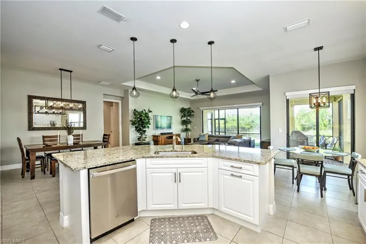 Kitchen featuring a tray ceiling, stainless steel dishwasher, a center island with sink, and sink