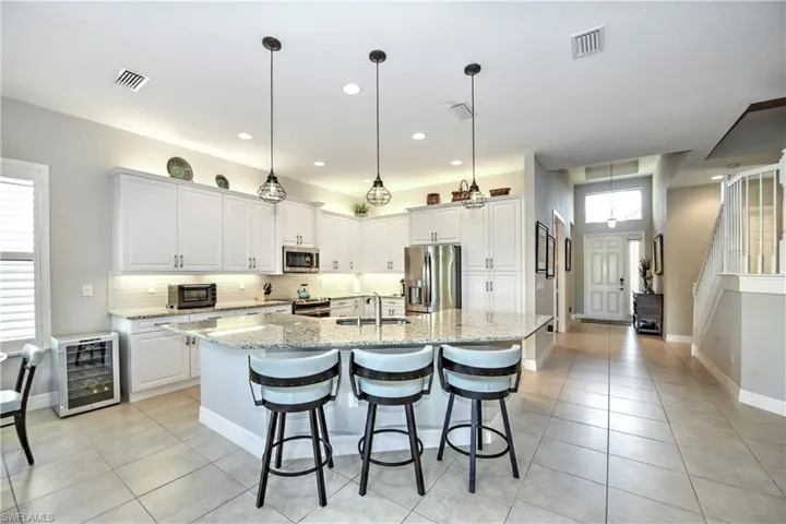 Kitchen with white cabinetry, beverage cooler, light stone counters, a center island with sink, and appliances with stainless steel finishes