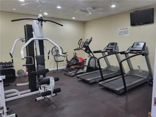 Gym with a ceiling fan, a paneled ceiling, and baseboards