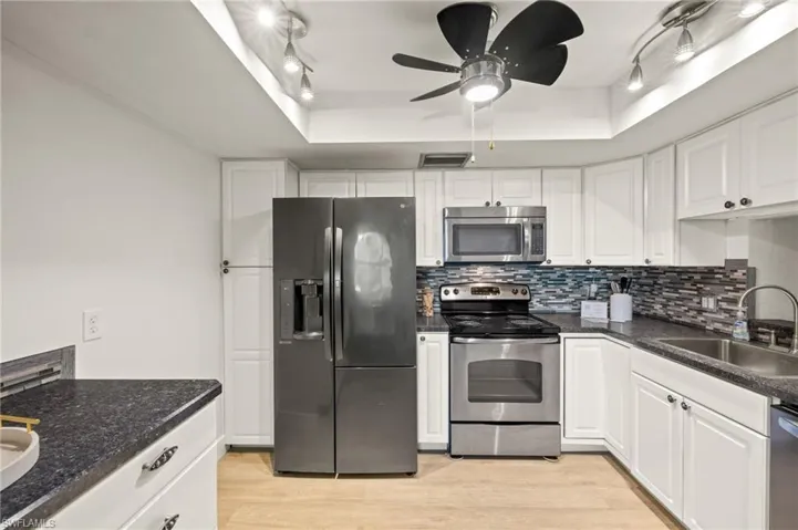 Kitchen with stainless steel appliances, rail lighting, a sink, a tray ceiling, and backsplash