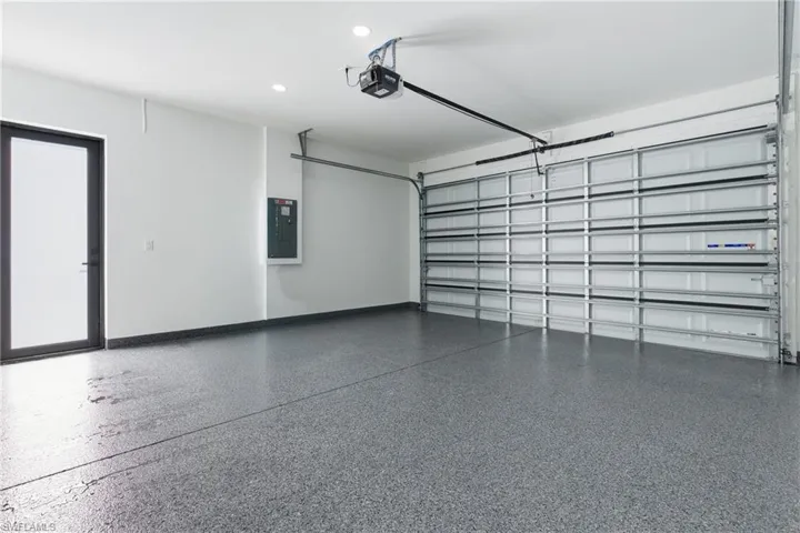 Garage featuring electric panel, a garage door opener, and recessed lighting