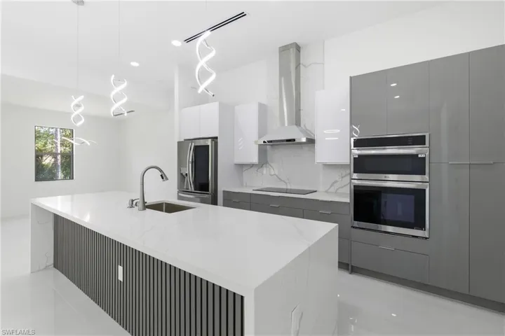 Kitchen featuring modern cabinets, two tone cabinets, stainless steel appliances, light stone counters, and decorative light fixtures