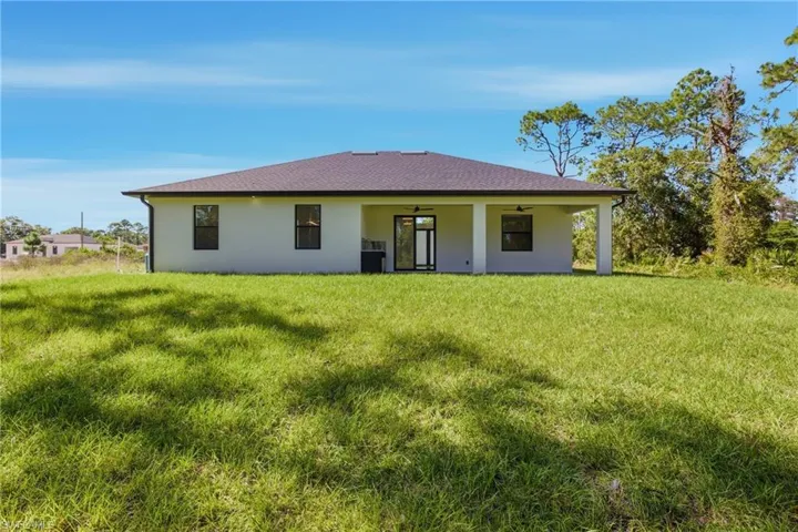 Rear view of property featuring ceiling fan, stucco siding, a patio, a lawn, and roof with shingles
