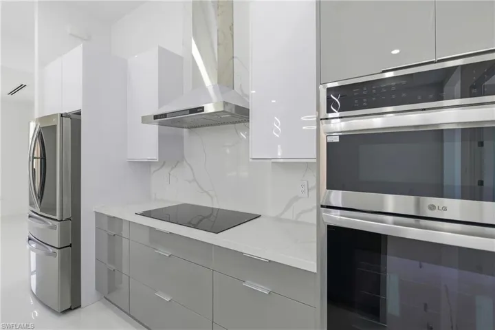Kitchen with modern cabinets, stainless steel appliances, decorative backsplash, gray cabinets, and light stone countertops