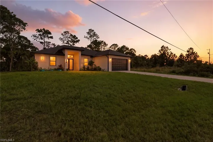 View of front of house with concrete driveway, stucco siding, a front yard, and an attached garage