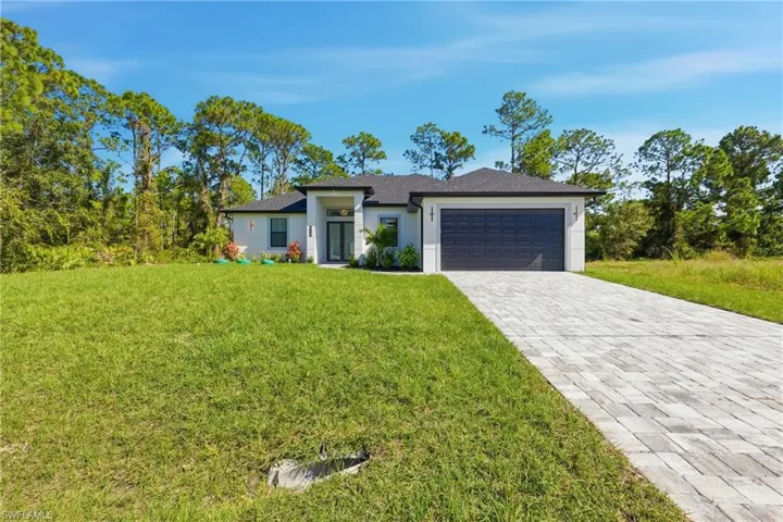 Prairie-style house with a front yard, decorative driveway, a garage, and stucco siding