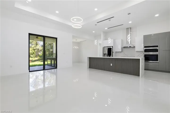 Kitchen with modern cabinets, a large island with sink, decorative light fixtures, stainless steel appliances, and light stone countertops