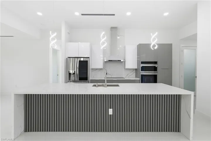 Kitchen featuring modern cabinets, light stone counters, tasteful backsplash, white cabinets, and hanging light fixtures
